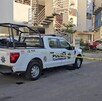 Patrulla de la Policía de Tlajomulco sosteniendo una cinta policiaca que acordona la calle afuera de edificios de departamentos con autos alrededor