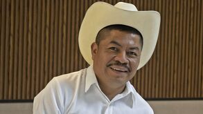 Hombre con sombrero y atuendo en color blanco posa para una fotografía.