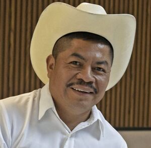 Hombre con sombrero y atuendo en color blanco posa para una fotografía.