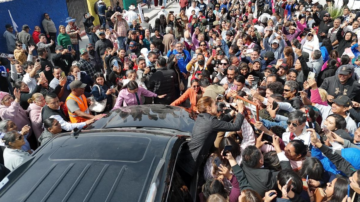 Una gran multitud se acerca al vehículo de la presidenta Claudia Sheinabum, que se asoma por la ventana para saludar a los presentes.