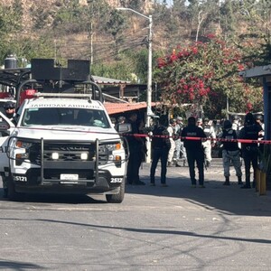 Camioneta de la Guardia Nacional con las puertas abiertas y oficiales y militares a un lado vistos de espaladas detrás de un área acordonada