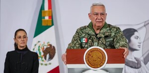 Ricardo Trevilla Trejo, titular de la Sedena, hablando delante de un podio con un micrófono y Claudia Sheinbaum en el fondo