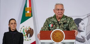 Ricardo Trevilla Trejo, titular de la Sedena, hablando delante de un podio con un micrófono y Claudia Sheinbaum en el fondo