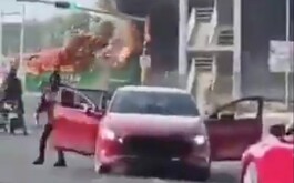 Vehículo en color rojo y camión incendiandose de fondo