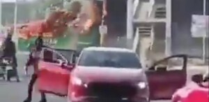 Vehículo en color rojo y camión incendiandose de fondo