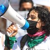 Mujer marcha cubierta del rostro y con un megáfono sobre la mano.