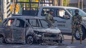 Militares parados junto a un auto calcinado en calles de Jalisco.