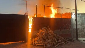 Exterior de una carpintería con llamas y columnas de fuego dentro y una pila de palos de madera en el suelo