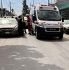 Se observa una camioneta tipo ambulancia, unos vehículos en vía pública y personas.