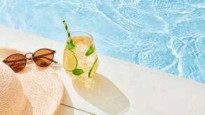 Unos lentes de sol, un sombrero y una bebida a la orilla de una piscina con agua cristalina