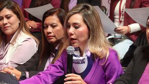 Mujeres vestidas en color morado en una conferencia de prensa.