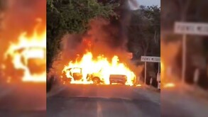 Vehículos envueltos en llamas bloqueando una carretera de Autlán de Navarro con árboles alrededor