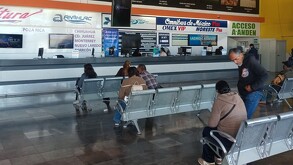 Se observan a personas sentadas dentro de una central de autobuses.