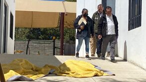 Personas caminando junto a los cuerpos de dos niñas muertas en el DIF de Oaxaca.