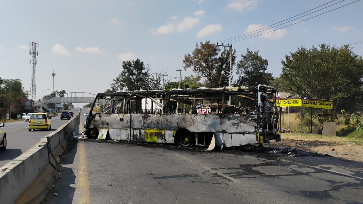 Camión de transporte público calcinado en medio de una carretera de Jalisco frente a una llantera y con autos circulando a un costado