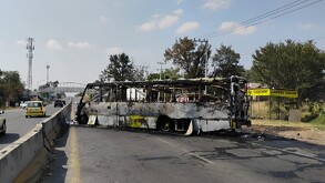 Camión de transporte público calcinado en medio de una carretera de Jalisco frente a una llantera y con autos circulando a un costado