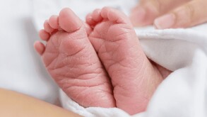 Se observan los pies de un recién nacido, tapado con una cobija.