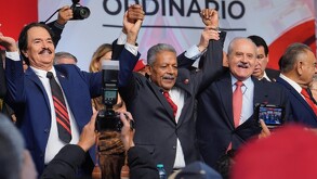 Se observa a tres hombres con las manos hacia arriba, traen traje con corbata.