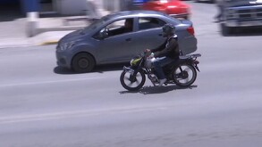 Se observa un motociclista con casco transitando sobre una vía, también se observa un carro.
