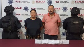 Un hombre y una mujer con los ojos censurados por un recuadro borroso con dos oficiales de la Policía de Colima a los lados y una mesa roja con indicios delante
