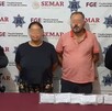 Un hombre y una mujer con los ojos censurados por un recuadro borroso con dos oficiales de la Policía de Colima a los lados y una mesa roja con indicios delante