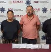 Un hombre y una mujer con los ojos censurados por un recuadro borroso con dos oficiales de la Policía de Colima a los lados y una mesa roja con indicios delante