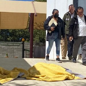 Personas caminando junto a los cuerpos de dos niñas muertas en el DIF de Oaxaca.