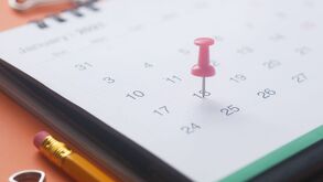 Un calendario sobre una mesa, marcado en la casilla de una fecha con un tachuela de color rosa