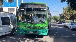 VIsta del frente de un camión verde de la ruta 612 en Guadalajara estacionado en medio de la calle al lado de una van blanca y autos alrededor