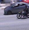 Se observa un motociclista con casco transitando sobre una vía, también se observa un carro.