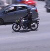 Se observa un motociclista con casco transitando sobre una vía, también se observa un carro.
