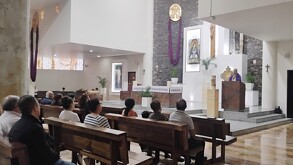 Personas sentadas dentro de  la Parroquia de Nuestra Señora de Altagracia durante una misa funeraria con un padre dando oración