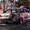Automóvil Volkswagen Jetta color gris calcinado y con el cofre levantado estacionado al exterior de una casa y con rastros de incendio en la calle