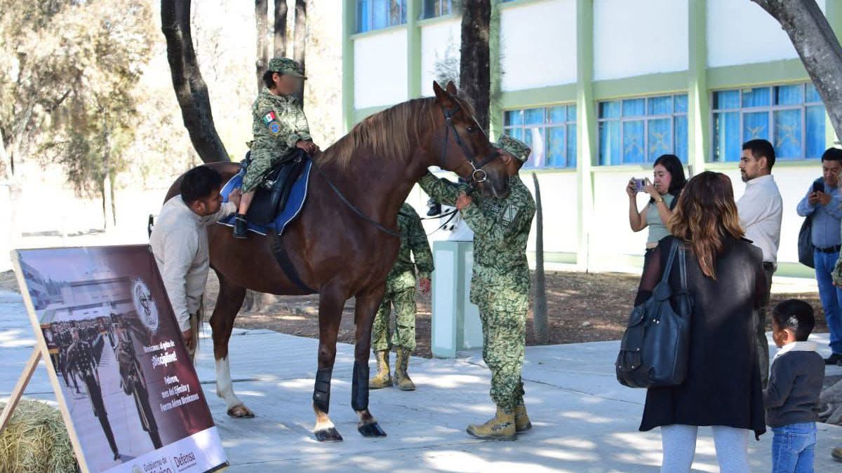 una niña con uniforme militar montando a caballo en una instalación del ejército mexicano