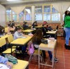 Maestra escribiendo en una pizarra blanca delante de un grupo de alumnos de educación básica adentro de un salón de clases