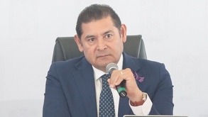 Hombre de traje sosteniendo un micrófono, mientras realiza un gesto de desagrado.