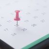 Un calendario sobre una mesa, marcado en la casilla de una fecha con un tachuela de color rosa