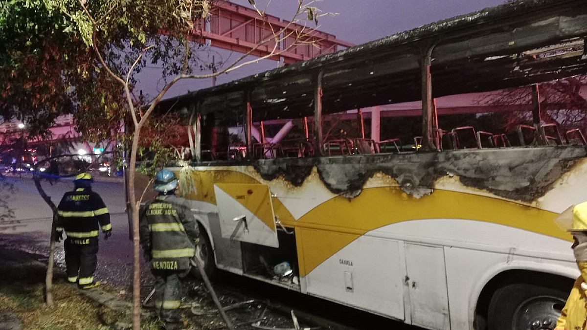 Camión de pasajeros calcinado sobre una carretera con Bomberos de Tlaquepaque a un lado
