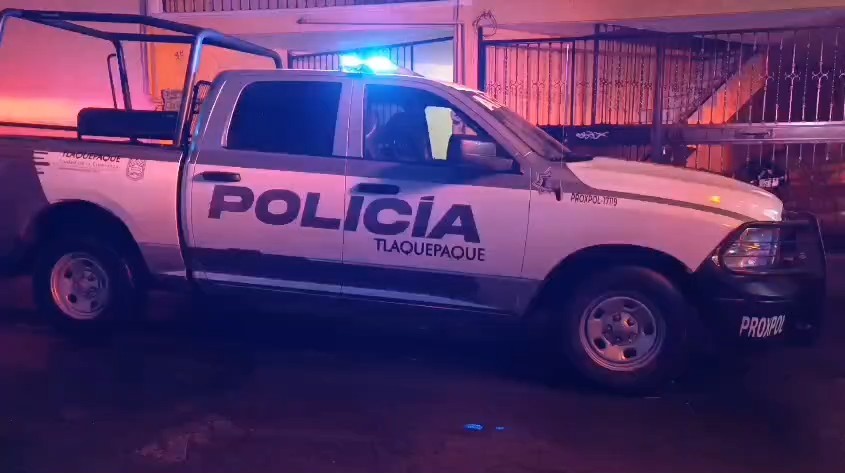 Patrulla de la Policía Municipal de Tlaquepaque con la sirena encendida estacionada al exterior de una casa con portón negro