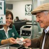 Adulto mayor sonriendo mientras recibe el pago de la pensión del IMSS a través de una ventanilla con una mujer haciendo la entrega de los billetes