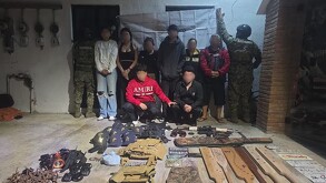 Cuatro hombres y cuatro mujeres con la cara blureada con dos oficiales de la Marina a los lados, además de armas y equipo táctico delante
