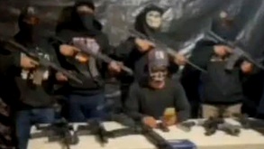 Personas armadas paradas detrás de un hombre que lee un mensaje.