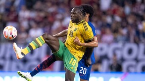 Jugador de la Selección de Fútbol de Jamaica pateando un balón en el aire con otro futbolista detrás de él