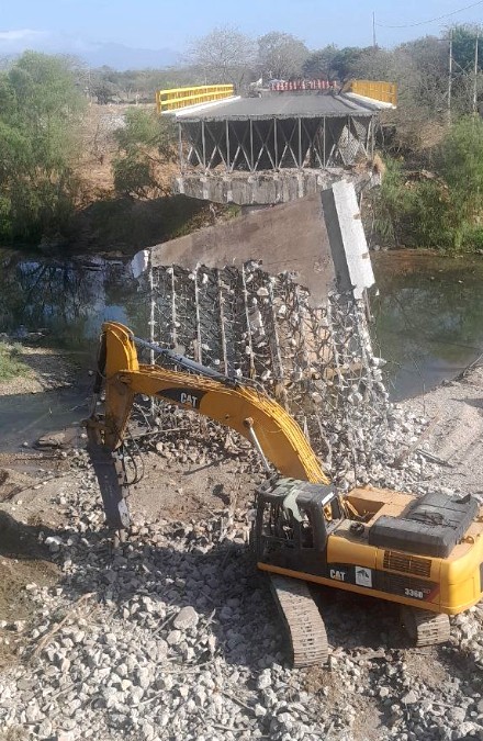 Taladro industrial al lado del Puente La Desembocada con un trozo demolido y trozos de concreto esparcidos sobre el suelo