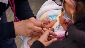 Se observa una bebé que está siendo vacunada, está cargada por una mujer.