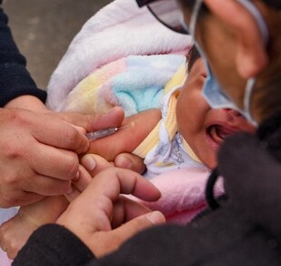 Se observa una bebé que está siendo vacunada, está cargada por una mujer.