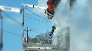 Trabajador colgando de un arnés de seguridad sujeto a una maquinaria industrial con fuego y humo desprendiéndose