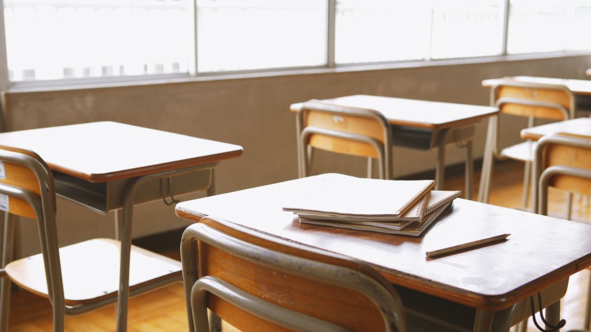 Un salón de clases con algunos asientos vacíos y en uno de ellos hay cuatro cuadernos apilados uno sobre otro y un lápiz