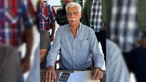 Samuel González Rodríguez sentado con una mesa, un celular y documentos al frente y tres hombres parados detrás de él