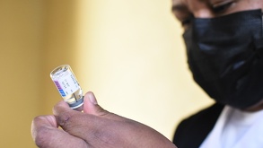 Una mujer con cubrebocas sostiene una jeringa con medicina.